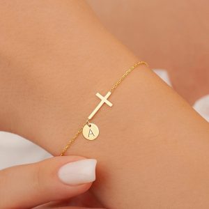 Gold-tone bracelet with round initial disc and cross detail on a wrist